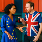 Future Flow Ein erkennbar diverses, britisches Ehepaar in modischer Kleidung und modischer Umgebung streitet in der Küche. Sie trägt ein Kleid in EU-Blau mit Sternen, er trägt ein Union-Jack-T-Shirt.