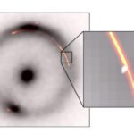 Der schwarze Ring und der zentrale Punkt zeigen das Infrarotbild einer fernen Galaxie, deren Licht durch eine Gravitationslinse verzerrt wird. Orange und Rot markieren Radiowellen desselben Objekts. Die Einblendung zeigt eine kleine Einbuchtung – verursacht durch eine weitere, deutlich kleinere dunkle Gravitationslinse (weißer Fleck).